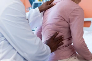 Doctor placing hands on a patient’s lower back during a clinical exam, illustrating evaluation for herniated disc or chronic back pain.