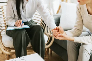 A patient sitting across from a pain specialist who is taking notes on a clipboard during a chronic pain consultation at Augusta Pain Center