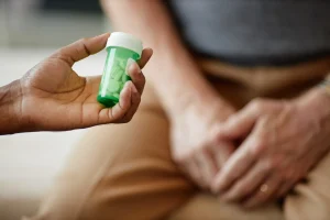 Person holding a prescription pill bottle while resting a hand on a sore knee, illustrating the limits of relying on pain medication alone for chronic pain management.