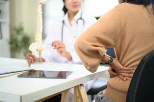 Woman holding her lower back in pain while consulting with a pain management specialist who is explaining radiofrequency ablation.